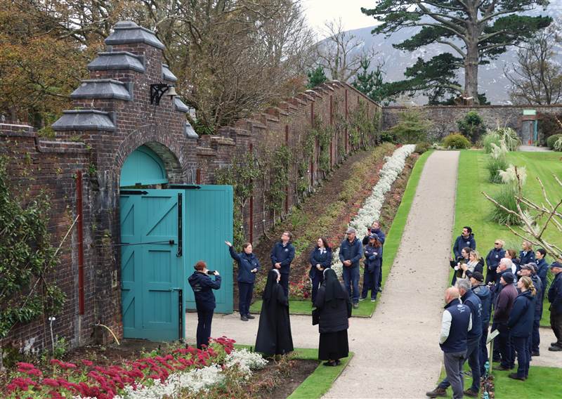 People looking at garden bell hanging on a stone wall